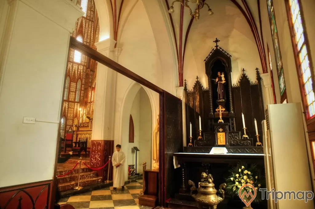có 1 người mặc áo trắng đang đứng, bàn thờ có bức tượng Đức Mẹ đang bế chúa giêsu và có 4 cây nên trắng và 1 cây thập giá, có 1 cái lư hương đồng và 1 chậu hoa